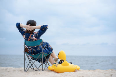 Woman relax and sit on beach chair with her cat sit on duck rubber ring on sand beach