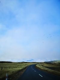 Scenic view of road amidst field against sky