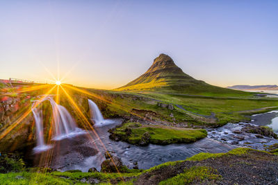 Scenic view of waterfall and landscape against sky during sunset