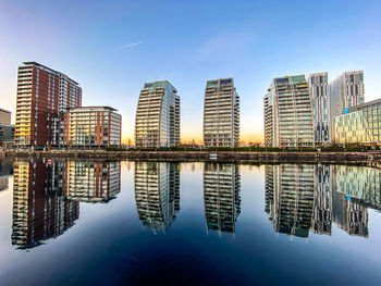 Reflection of buildings in city against clear blue sky