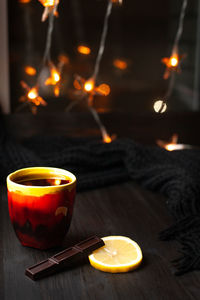 A mug of tea with slice of lemon and dark chocolate on a background with christmas lights