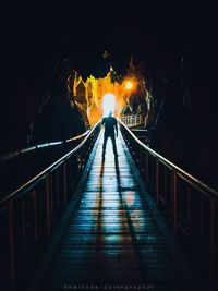 Rear view of man standing on footbridge at night