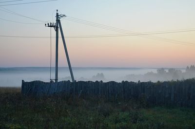 Electricity pylon on land against sky during sunset