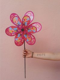 Cropped hand of girl with hope text holding pinwheel against wall