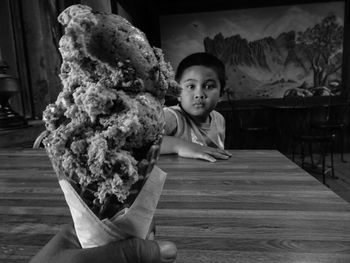 Cropped hand holding ice cream in front of boy at restaurant