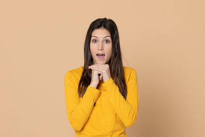 Portrait of young woman standing against yellow background