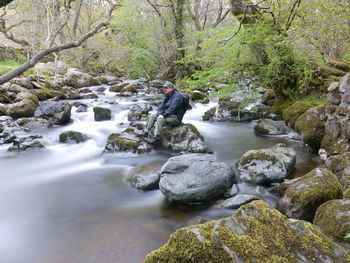 Man sitting on rock amidst stream in forest