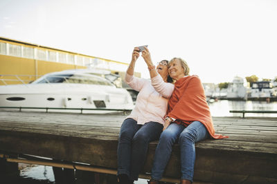 Senior women taking selfie through mobile phone while sitting on pier