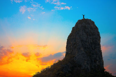 Low angle view of silhouette person on rock against sky during sunset