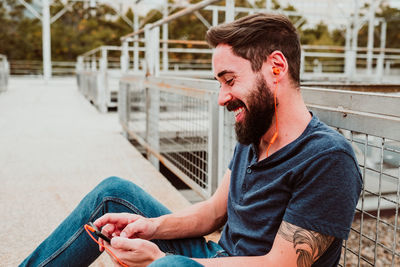 Young man looking away while sitting on railing