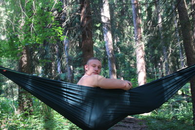 Portrait of smiling man sitting on hammock in forest