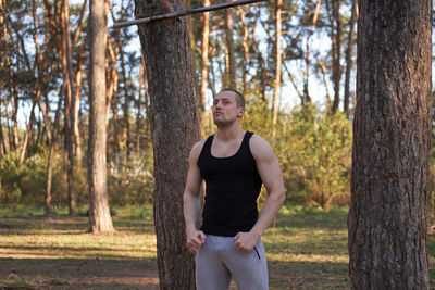 Young man standing by tree trunks in forest