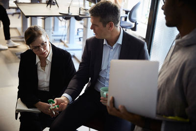 Male entrepreneur holding laptop while bank managers discussing over solar toy car during meeting in creative office