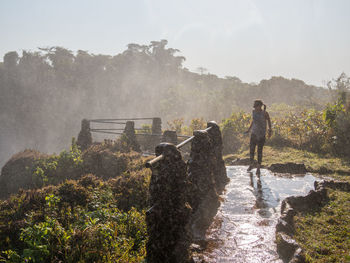 Woman walking on footpath with spray of lumangwe falls, zambia