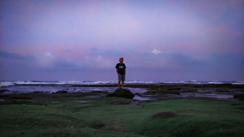 Rear view of man standing on beach against sky during sunset