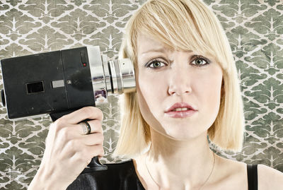 Portrait of woman holding video camera against wall