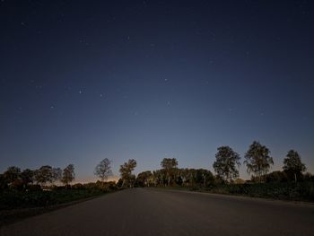 Empty road amidst trees against sky at night