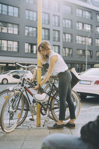 Full length of businesswoman locking bicycle on sidewalk in city