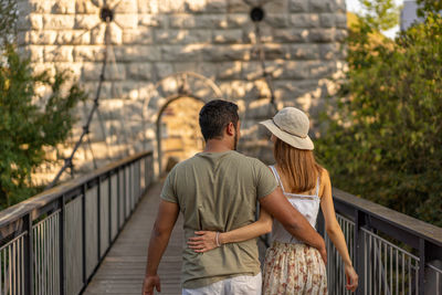 Rear view of couple walking on footbridge outdoors
