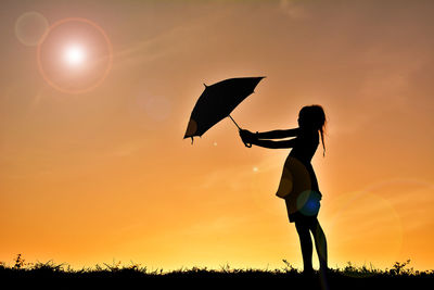 Low angle view of silhouette girl holding umbrella on field against sky during sunset