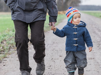 Midsection of grandfather with granddaughter walking on dirt road