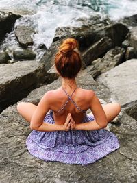 Rear view of woman exercising while sitting on rock