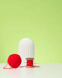 Red ball with woolen thread and large needle on white table, green background