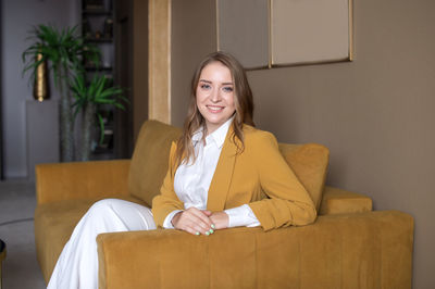 A successful girl in the office is sitting on the sofa in an olive jacket and smiling