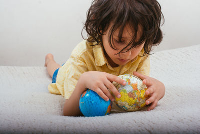 Boy holding globe while lying down on bed