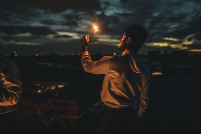 Rear view of man and woman standing against sky at sunset