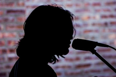 Side view of silhouette singer by microphone against brick wall
