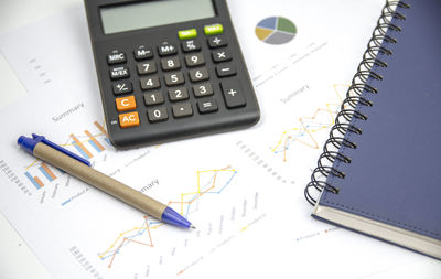 High angle view of graphs with diary by calculator and pen on table in office