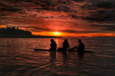 Silhouette friends on rowboat in river during sunset