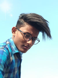 Portrait of young man wearing eyeglasses against blue sky