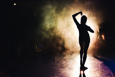 Silhouette of a woman dancing between lights and smoke unrecognozible person