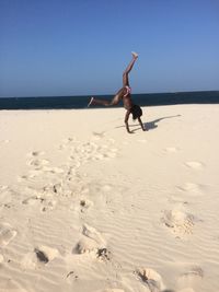 Full length of woman doing handstand on sea shore at beach against clear sky