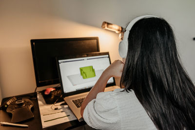 Rear view of young businesswoman sitting at desk, using laptop and 3d design software