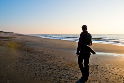 Rear view of man on beach against clear sky