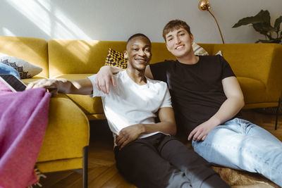 Portrait of smiling young man sitting with arm around friend at home