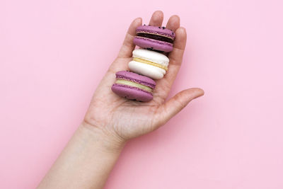 Cropped hand of woman holding macaroons over pink background