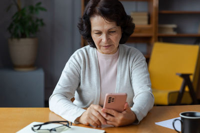 Young woman using mobile phone while sitting on table