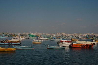 Boats moored at harbor in city against sky