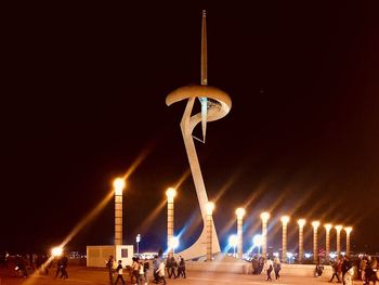 People at illuminated street light against clear sky at night