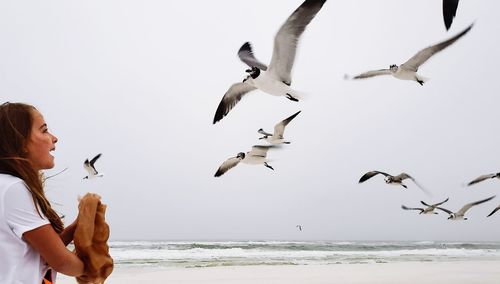 Girl looking at birds flying over sea