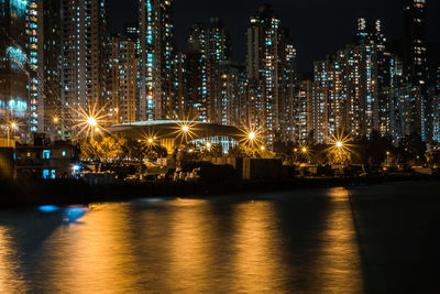 Illuminated buildings by river against sky at night