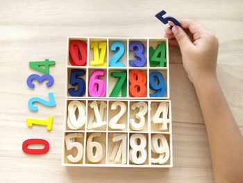 Cropped hand of child arranged colorful toy blocks in box on wooden table