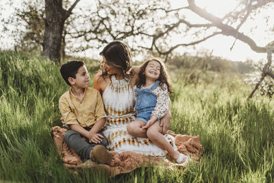Mother, son, and daughter in backlit field smiling at each other