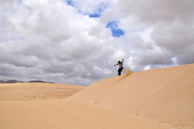 Woman on sand dune in desert against sky