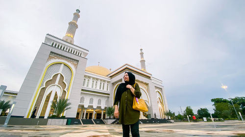 A veiled woman against the background of the great mosque of al-falah mempawah.