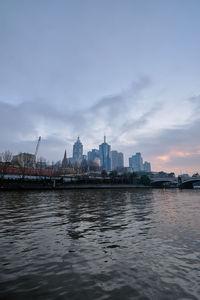 View of buildings by river against sky at dawn.